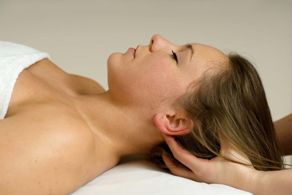 Eine Frau wird am Nacken massiert, dabei liegt sie auf dem Rücken. Man sieht nur die Hände der Masseurin.